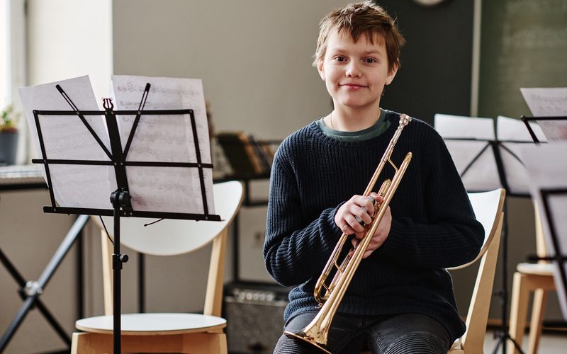 A young pupil holding a trumpet in a rehearsal room
