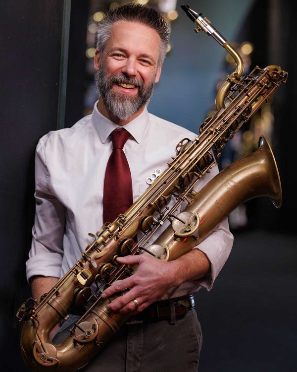 A smiling teacher holding a baritone saxophone