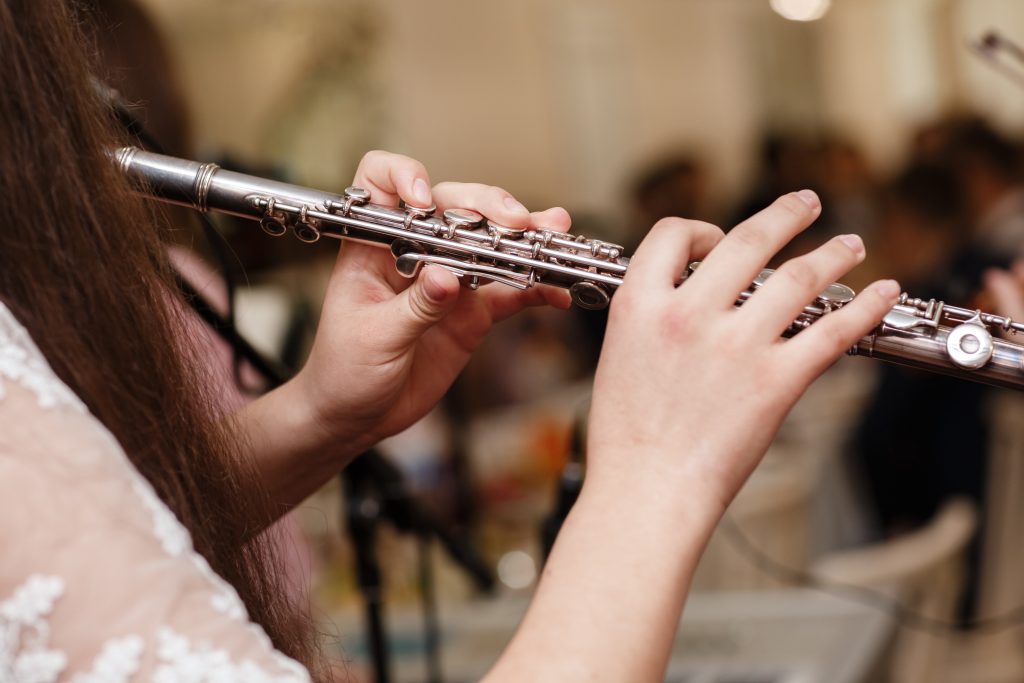 Flutist, young girl playing the flute, hands, fingers on keys closeup, children playing transverse side blow flute, detail shot, classical music, wind instrument performance player up close abstract.