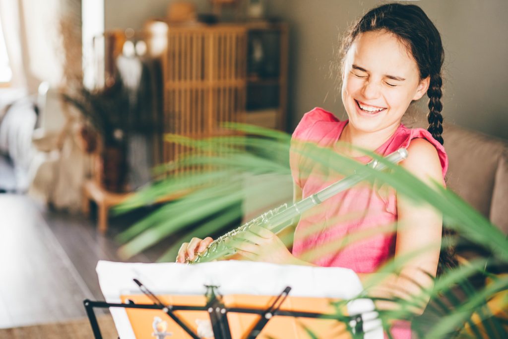 Young girl laughing, holding a flute looking at her music on the music stand. 