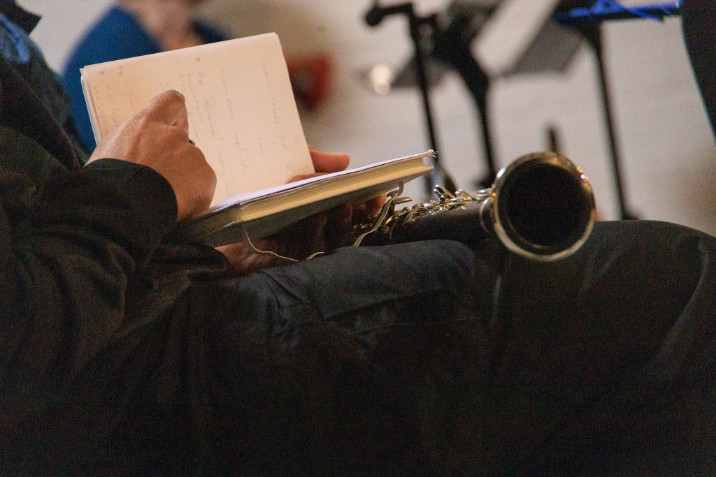 Person sat down with a clarinet resting on their lap whilst they write notes in a notebook